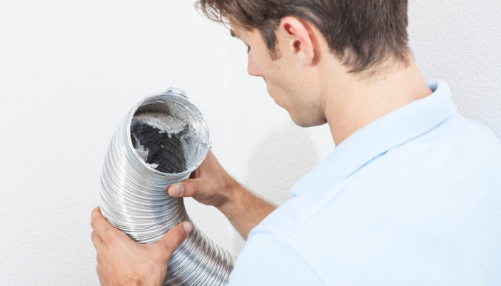 A man looks into a dirty dryer vent.