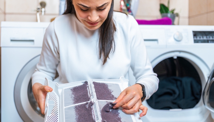 A woman cleans a dirty dryer lint trap.