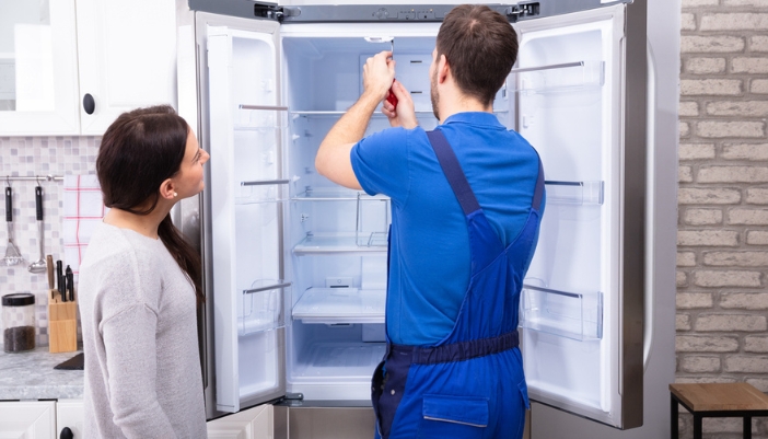 A woman observes a repair man working in her refrigerator.