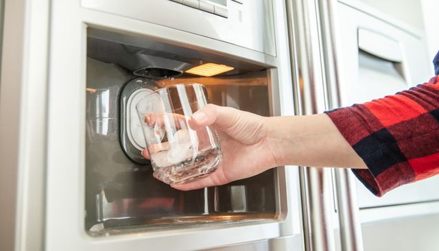 front view of a hand holding a cup trying to get ice out of an ice maker