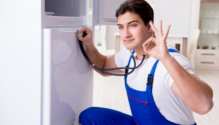 Service professional using a stethoscope to listen to the fridge