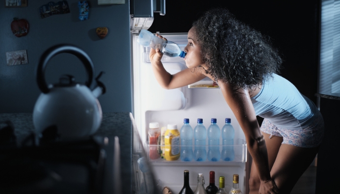 Woman taking a drink from a well-organized fridge