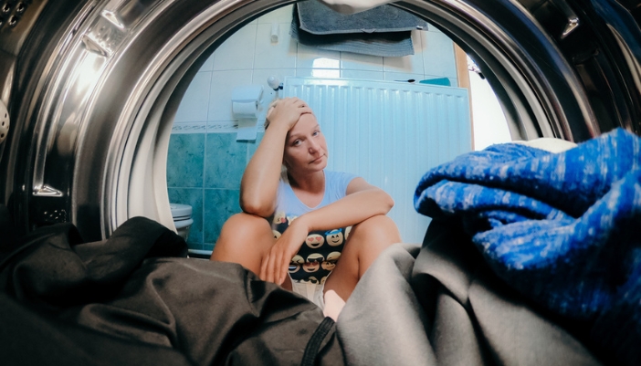 A frustrated woman sits in front of an open laundry appliance.