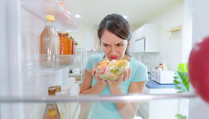Woman cautiously sniffing salad from the refrigerator