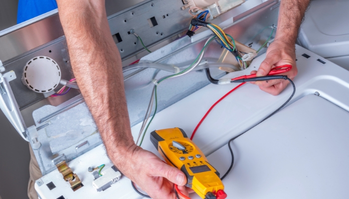 Appliance technician using electronic reader to diagnose washer wires