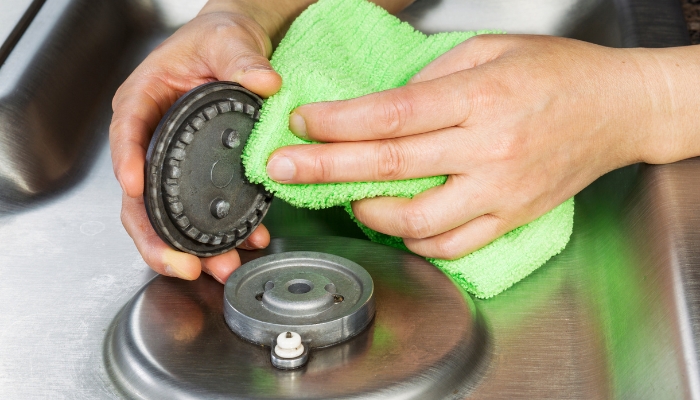 Serv_Gas-Burner-Troubleshooting_2.jpg Close-up of someone removing a gas burner cap and wiping things off near the electrodes