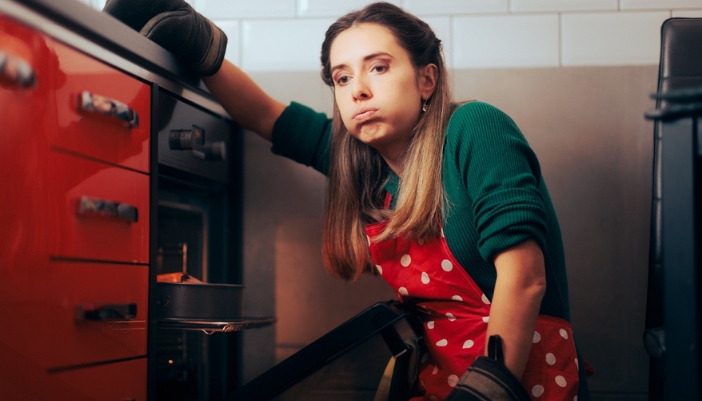 A frustrated woman in a red apron sits in front of a stove that is not working.