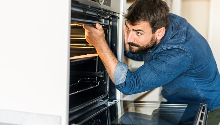 A man inspects the inside of a stove for problems and fixes.