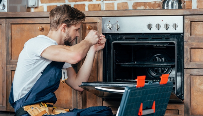 A repair technician fixes a stove in a natural wood kitchen.