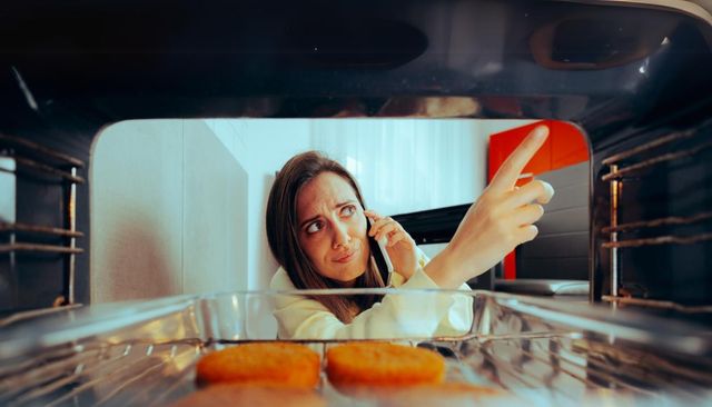 View from inside an oven of a woman on the phone and pointing at a problem with the oven