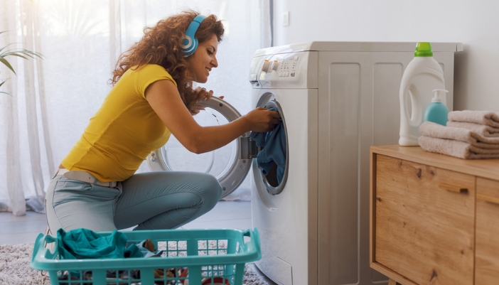 A young girl with headphones happily loads her washing machine.