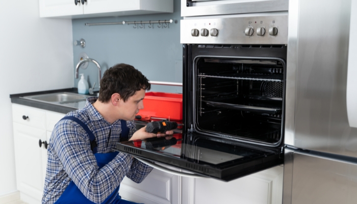 Serv_Appliance-Maintenance-Energy-Efficiency_4.jpg Service technician is screwing in loose parts of the oven door