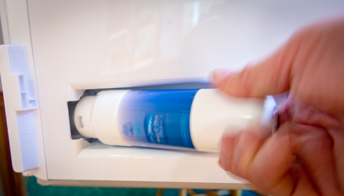 Closeup of someone replacing the water and ice filter in the fridge
