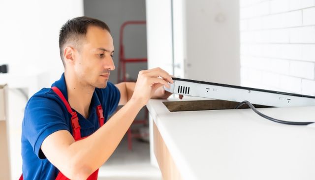 Side view of a man replacing a cooktop in a modern white kitchen