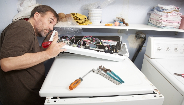 A man peering through wires of washer machine circuitry