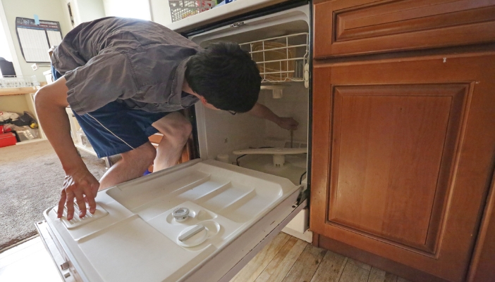 A young man screwing in something in a dishwasher