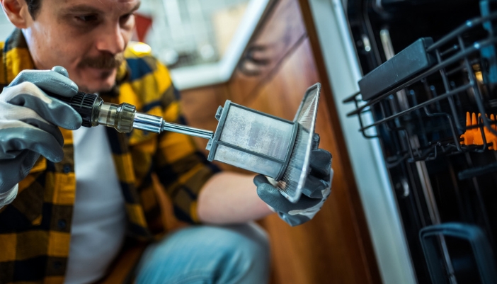 A man uses a screwdriver to fix a dishwasher filter.
