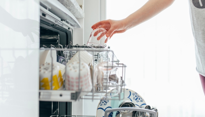 A woman’s hand loads cups and mugs into an open dishwasher.