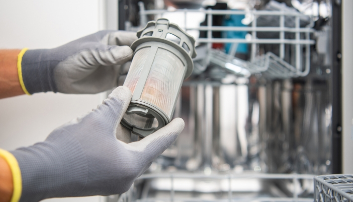 A pay of gloved hands removes and inspects a dishwasher filter.