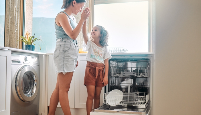 A mother and daughter high five after successfully doing a load of dishes.