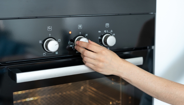 A delicate hand turns a knob on an oven to set the temperature.