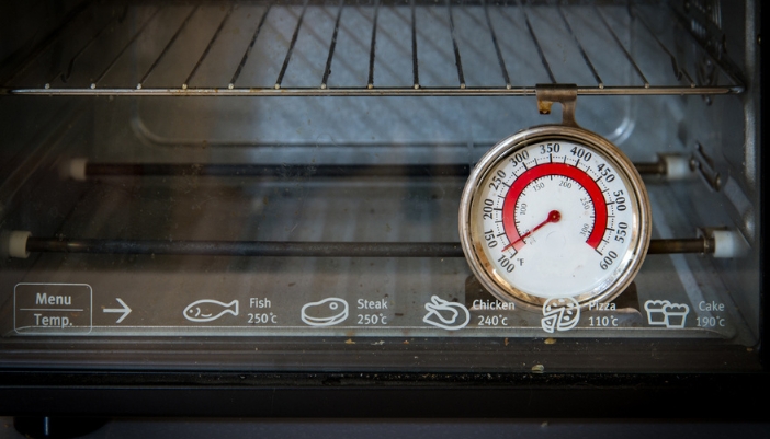 An older thermometer hangs from a rack in an open oven.
