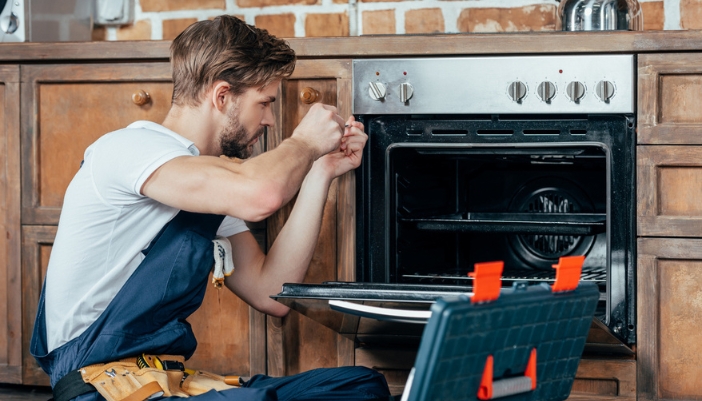 A young repairman uses a screwdriver to attempt to repair an oven.
