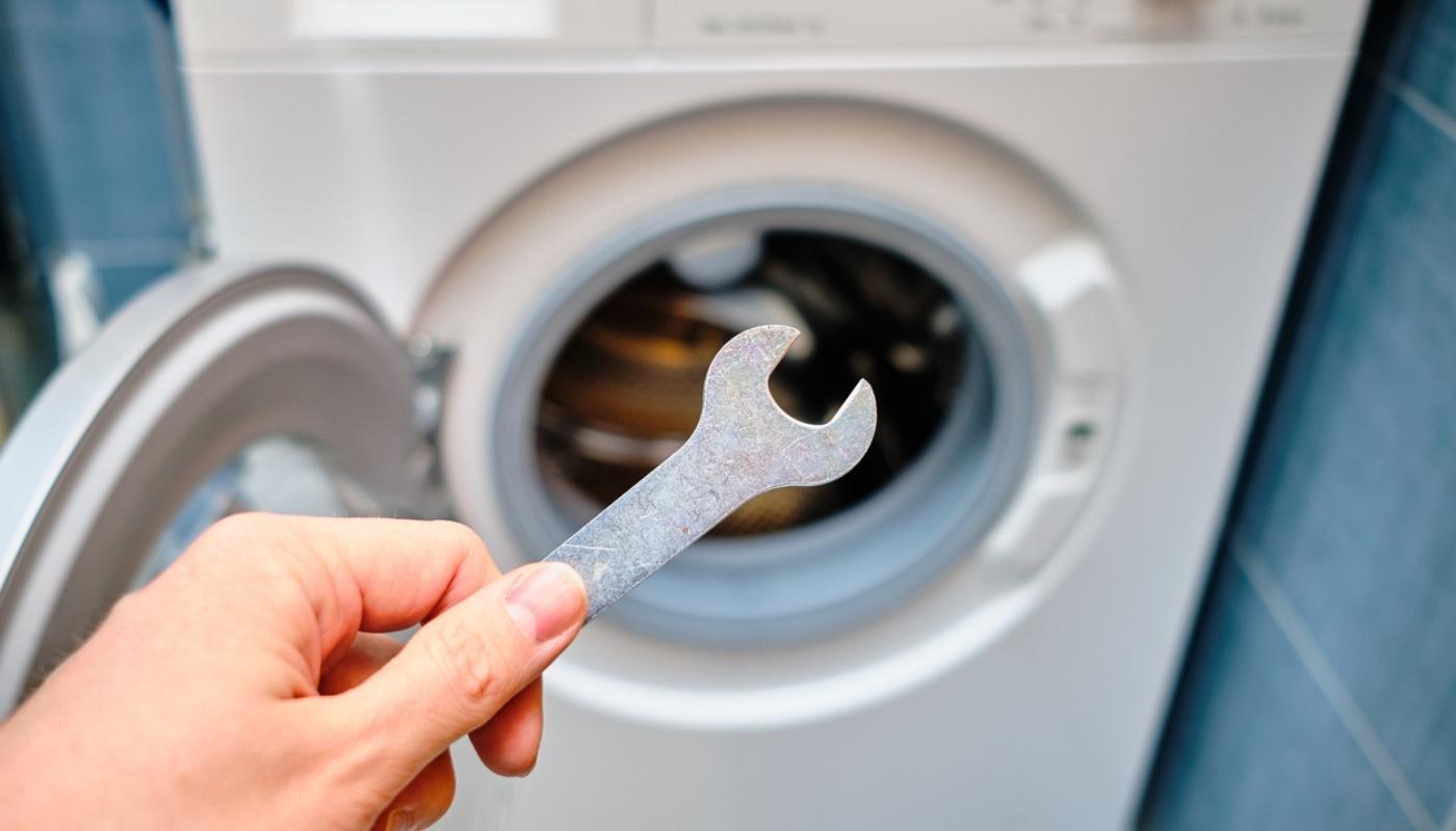 Person holding wrench in front of broken dryer