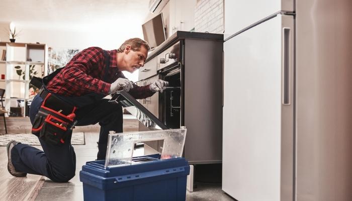 repairman examining oven with flashlight