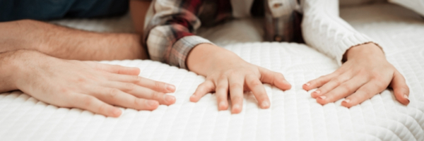 Three hands press down on a bare mattress.