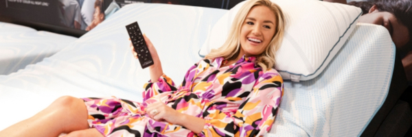 A woman lays on her bed in a brightly colored dress.