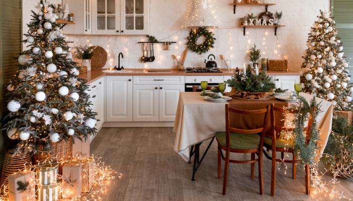 A dining room and kitchen decorated with white and greenery for the holidays. Lots of lights.