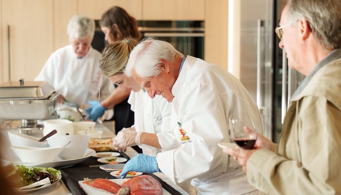 A diverse group of people in a Midland Appliance showroom kitchen, engaged in food preparation, showcasing teamwork and culinary skills.