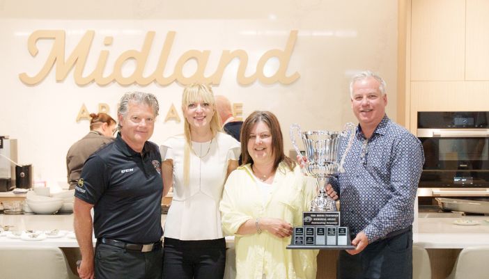 An individual holds a trophy with three people beside her in a Midland Appliance showroom kitchen.