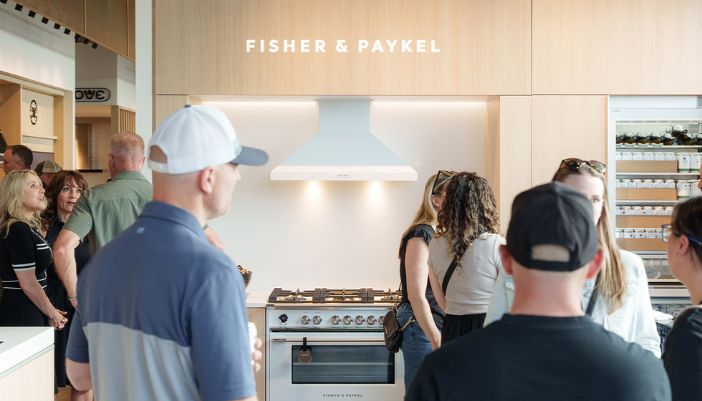 People gather in a modern Fisher & Paykel kitchen vignette within a Midland Appliance showroom that features sleek appliances and stylish cabinetry in a bright, inviting space.