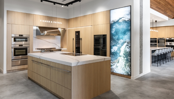Contemporary kitchen display at Midland Appliance showcasing Fisher & Paykel appliances, wood cabinetry, quartz island, and artistic wall feature.