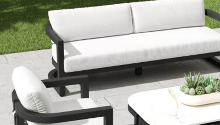 A set of white of black patio furniture on a gray patio with green grass.