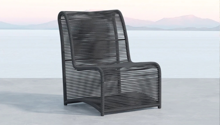 A black patio chair sits alone on a neutral, beachy background.