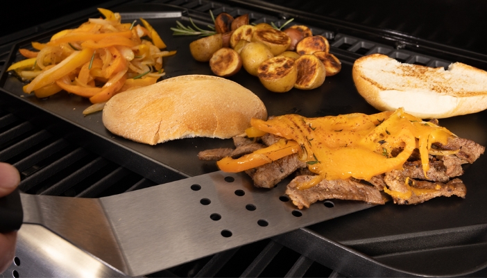 A griddle on a grill with a variety of foods cooking on it.