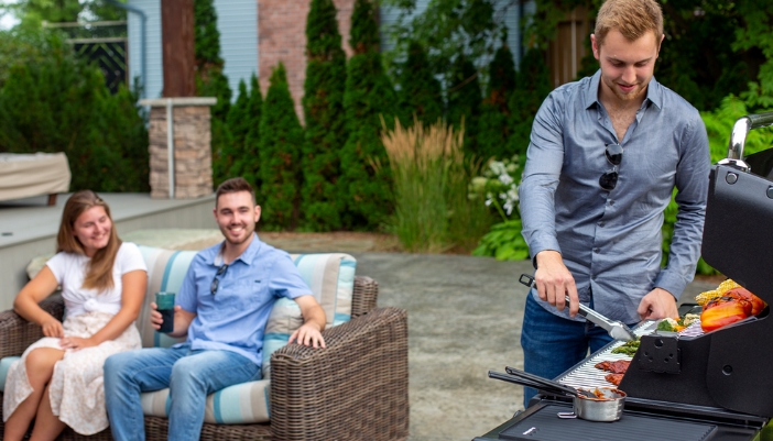 A group of friends sits outside on a patio and grills happily.