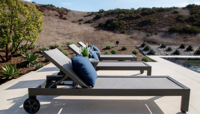 A set of flat patio pool chairs next to a pool on a bright day.