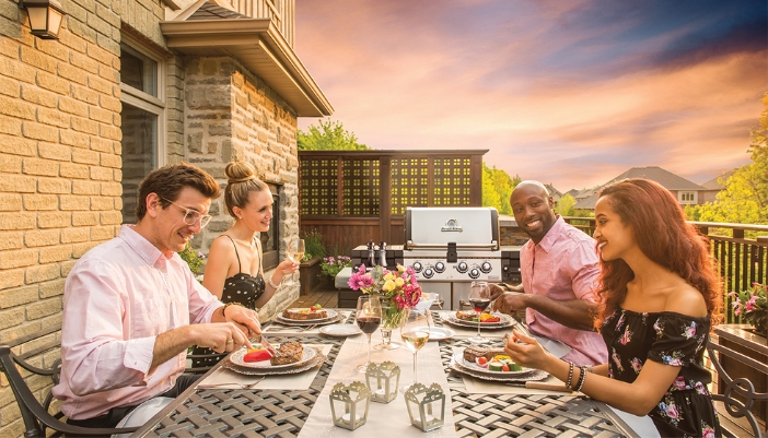 A group of friends sits at an outdoor table next to a grill. 