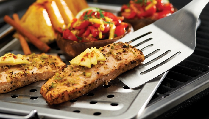 A close-up of fish and veggies roasting on a grill.