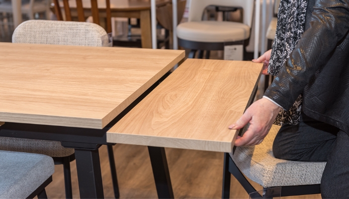 A pair of hands pulls out an extension for a dining table in a showroom.