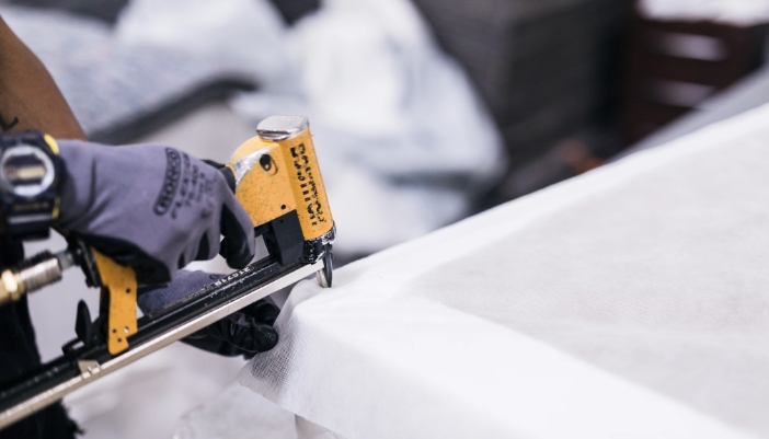 A man's hand holding a tool works on a mattress in a factory.