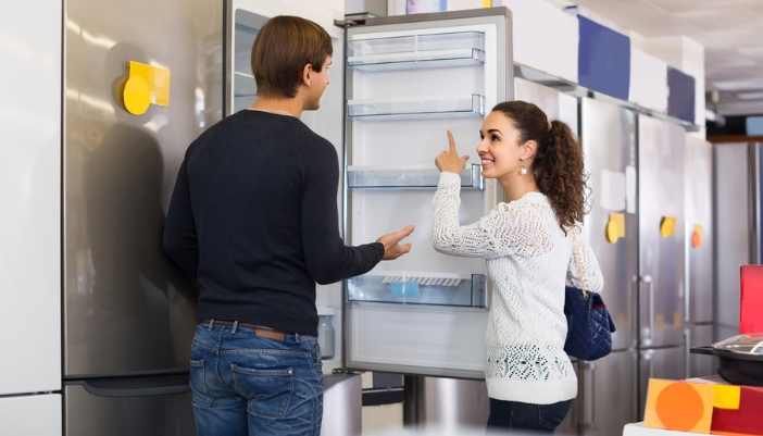 A couple opens a fridge in an appliance showroom.