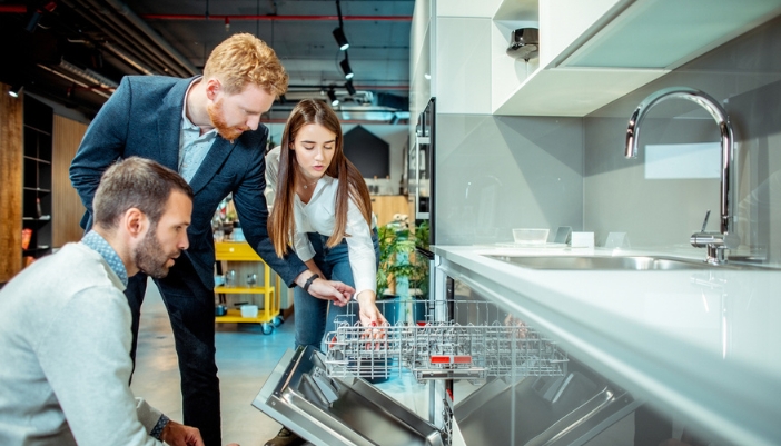 A man and woman work with a salesman in a suit to pick out a dishwasher.