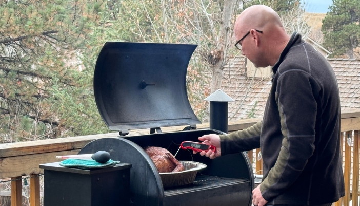 Man cooking turkey outside on grill