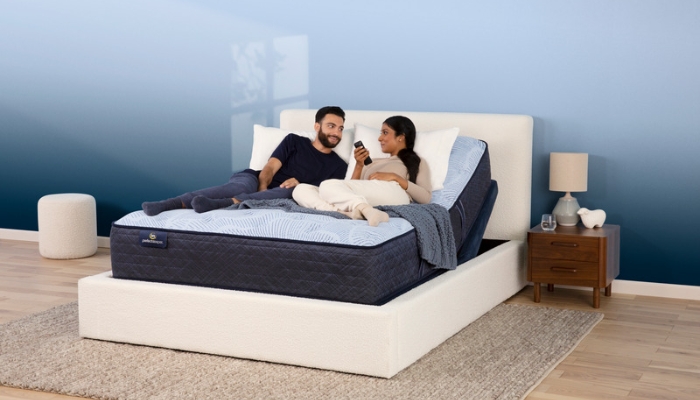 A couple lays on a blue adjustable base bed and the woman holds the remote