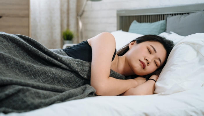 An Asian woman happily sleeps on her side.